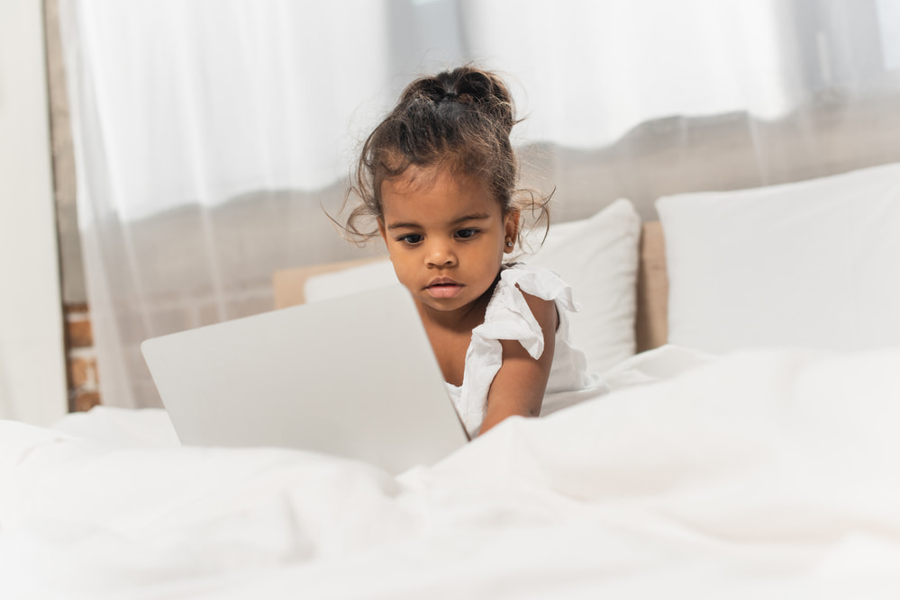 picture of toddler girl on bed playing on a laptop for a post on middle names for hazel