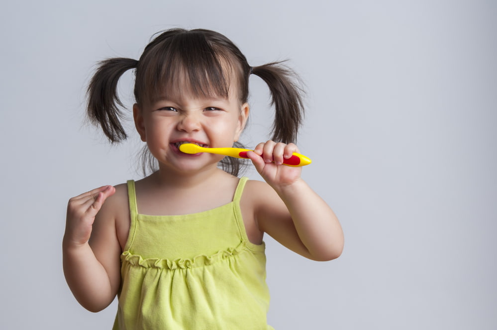 picture of toddler girl with pigtails brushing her teeth
