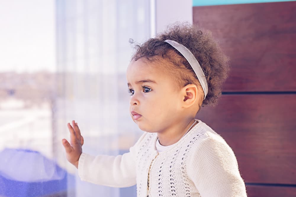 picture of toddler girl leaning against a window while she looks outside