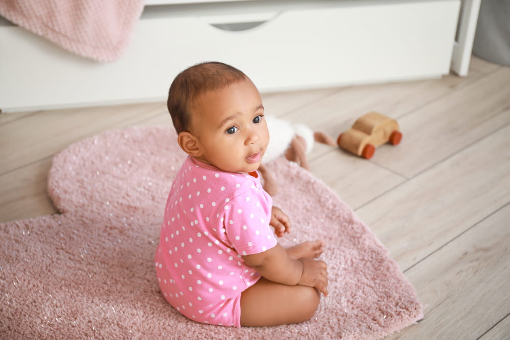 Picture of baby girl in pink onesie sitting on a pink heart shaped rug