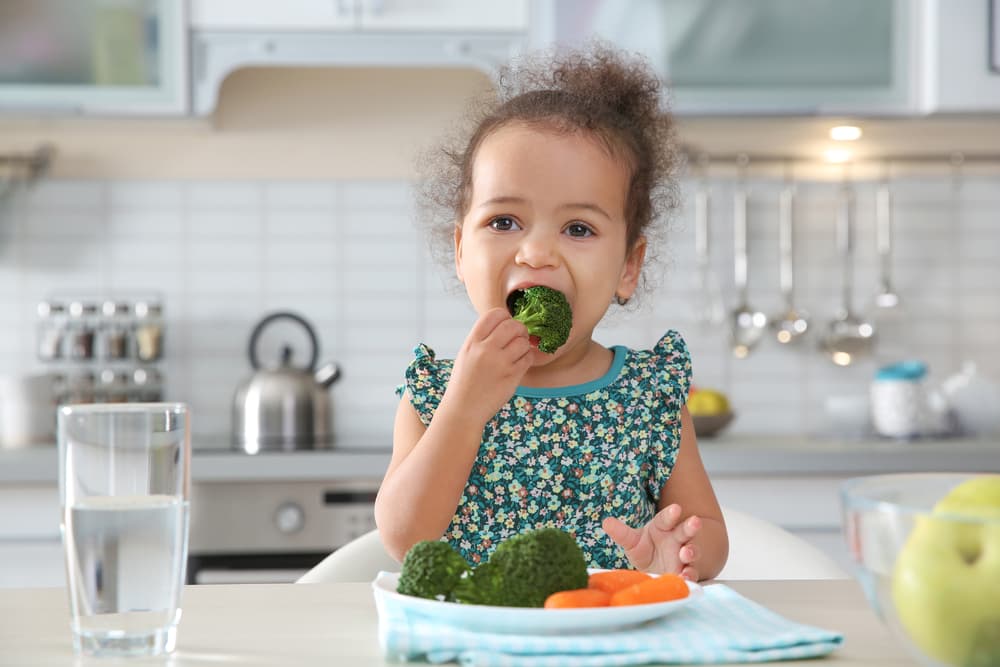picture of toddler girl in kitchen eating broccoli