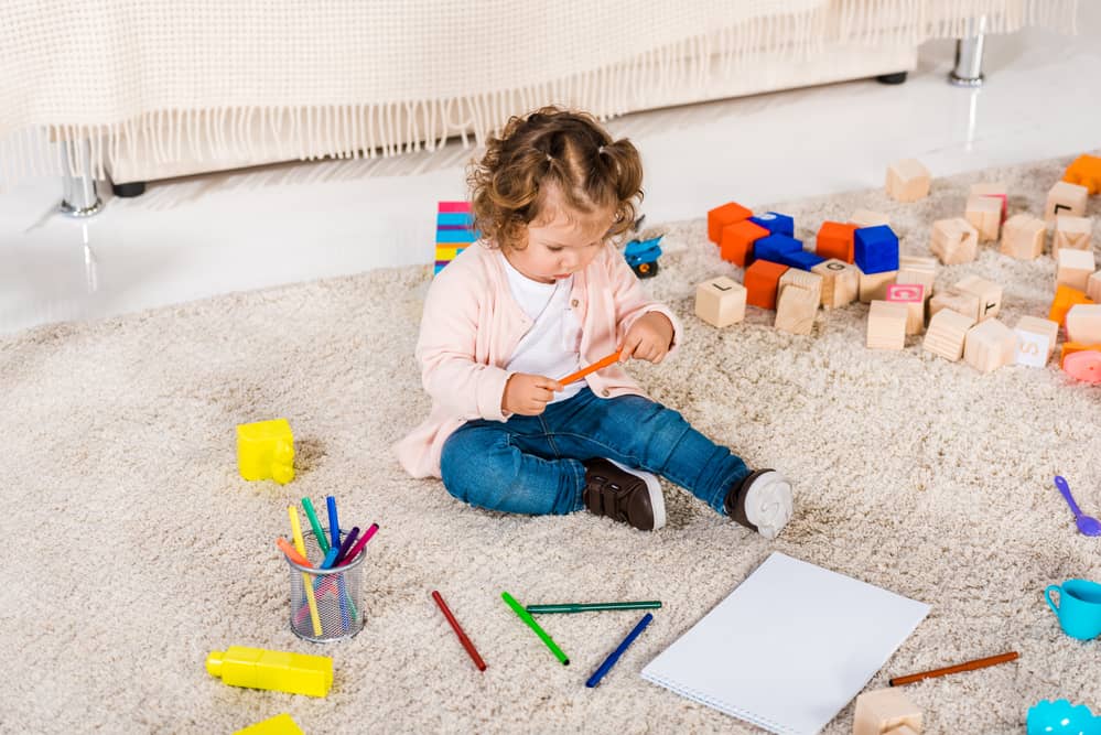 Picture of toddler girl on the floor playing with markers and surrounded by blocks