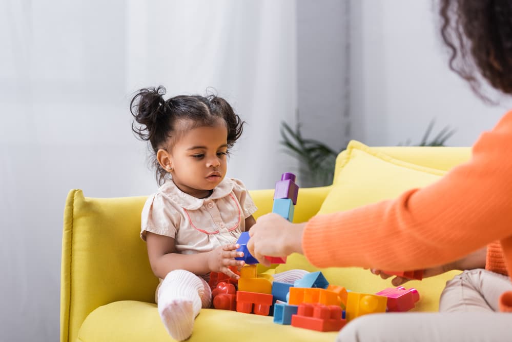 picture of toddler girl sitting on the couch playing with lego blocks