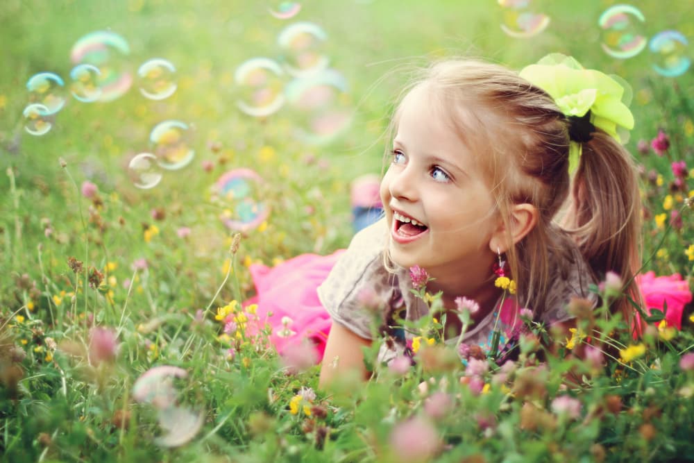 picture of little girl laying in a flower field with bubbles around her