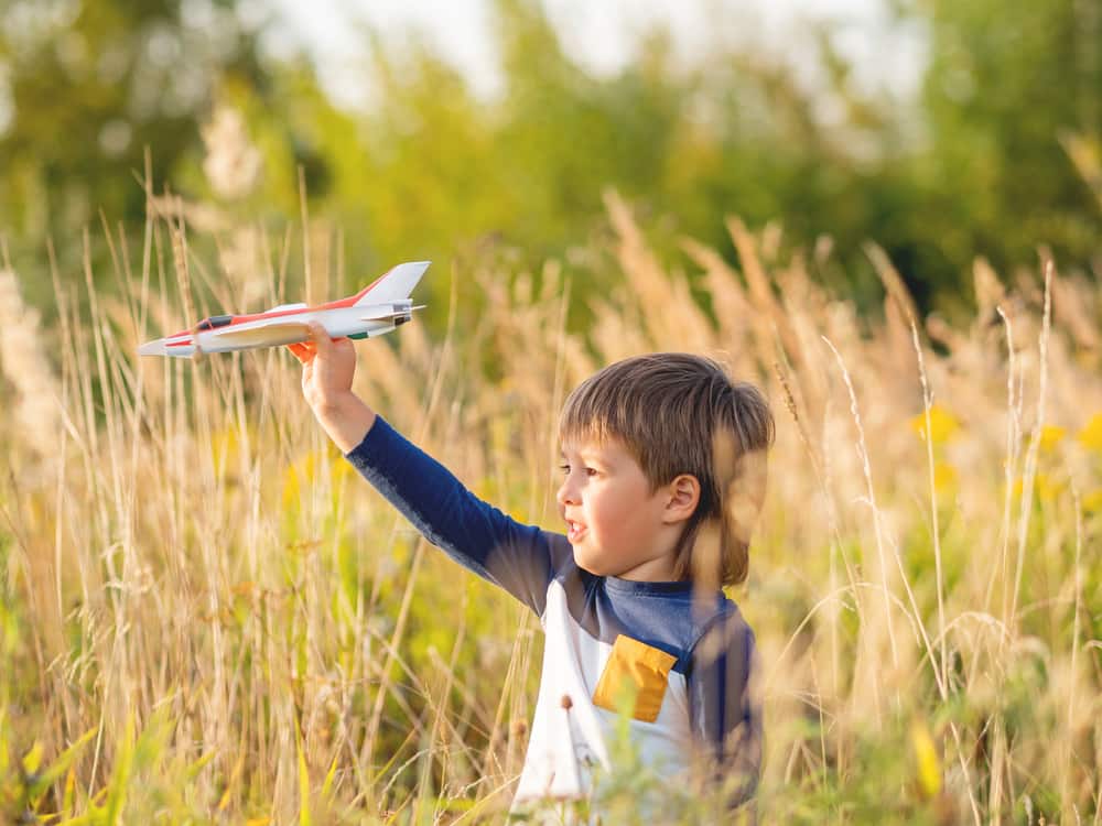 picture of little boy in field playing with toy airplane