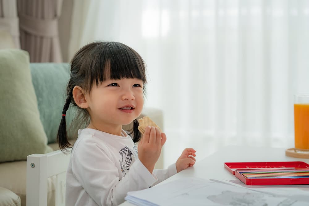 picture of toddler girl sitting at a table eating a snack