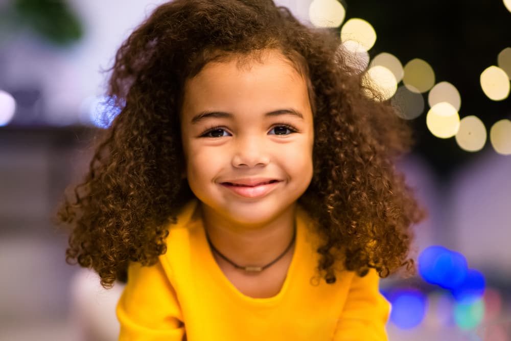 picture of toddler girl in yellow sweatshirt with lights sparkling in the background