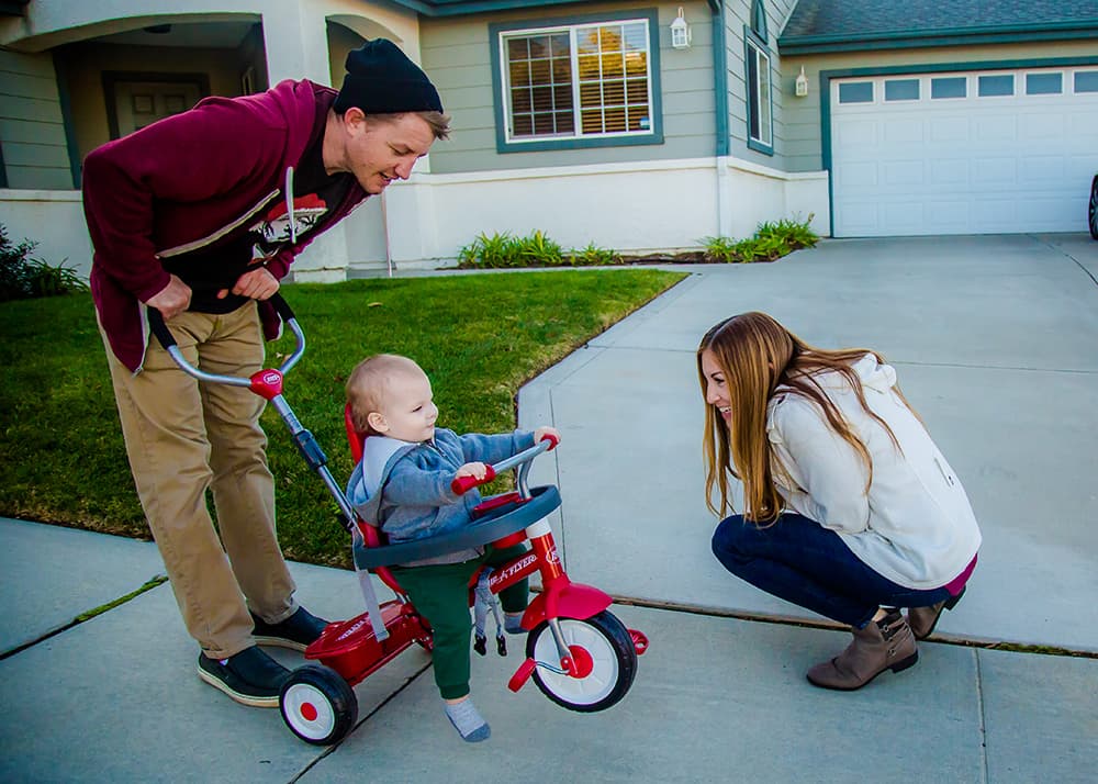 picture of mother and father with toddler on tricycle with push handle
