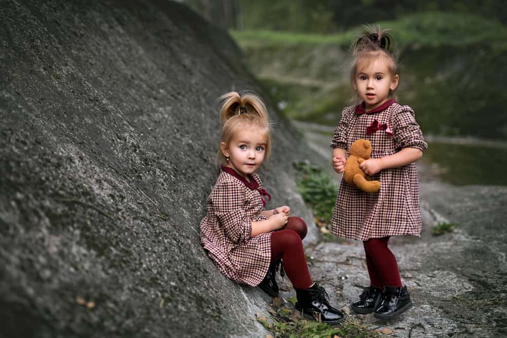 twin girls sitting next to rock outcrop
