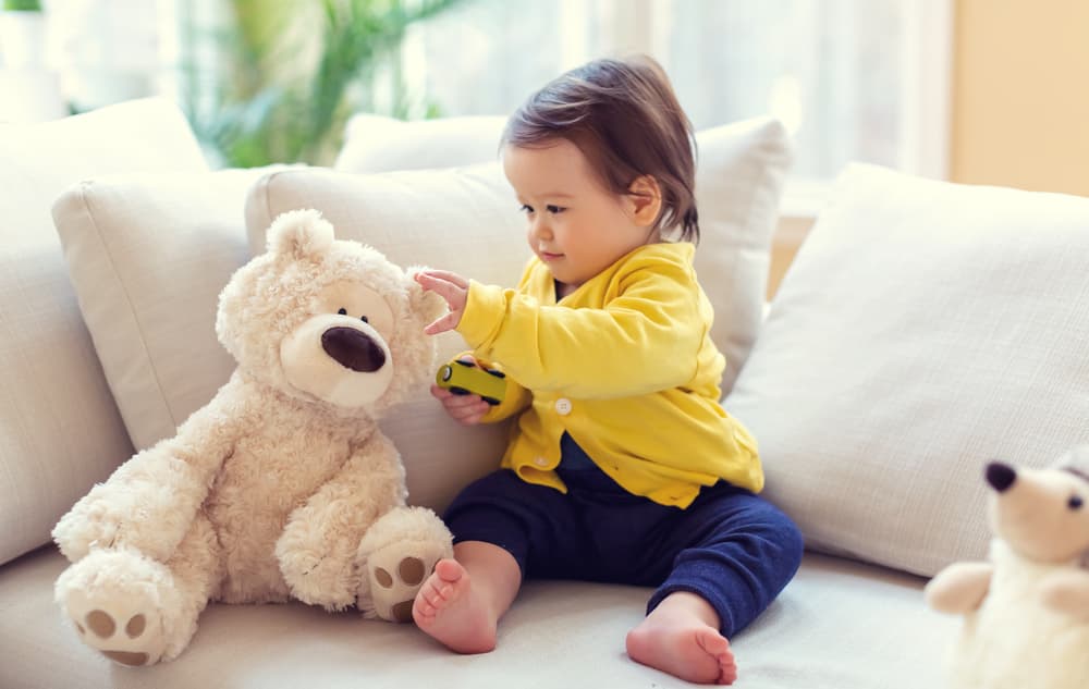 picture of baby boy on couch touching a stuffed animal bear
