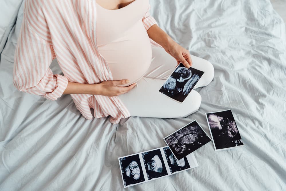 pregnant woman on bed holding ultrasound photos