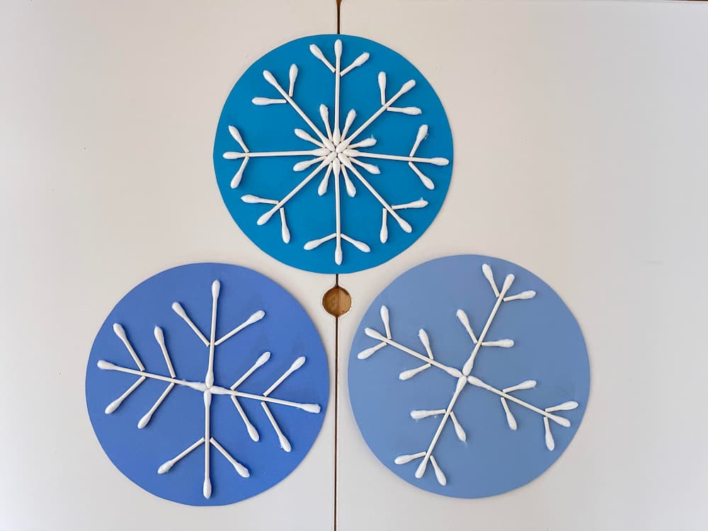 three q-tip snowflake crafts on blue card stock
