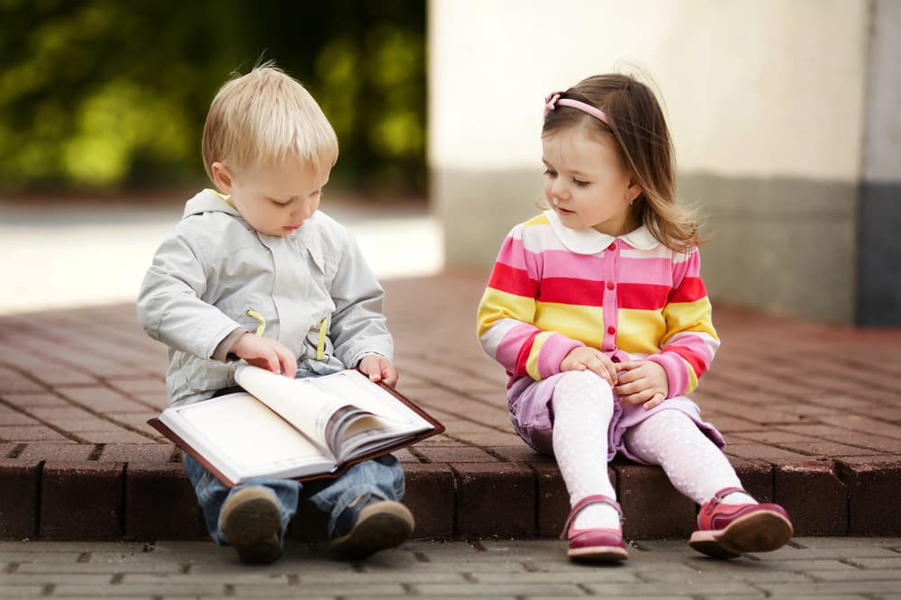 toddler boy and girl sitting down looking at a book